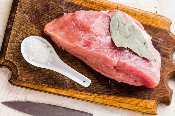 Pedazo de cerdo en una tabla de cortar, una hoja de laurel —  Fotos de Stock