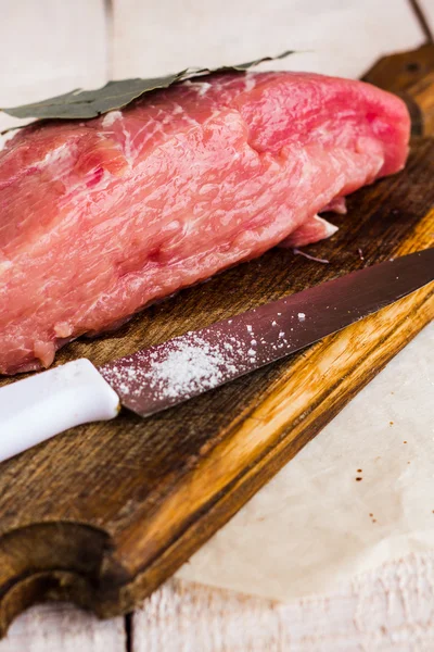 Χοιρινό σε ένα φύλλο δάφνης, το μαχαίρι και το αλάτι σε έναν ξύλινο πίνακα — Φωτογραφία Αρχείου