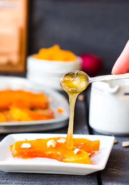 Лейте мёд на ложку запечённой тыквы с грецкими орехами, руками — стоковое фото