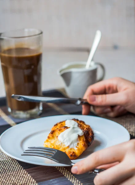 Comer panquecas de queijo coalhada com creme de leite para o café da manhã, mãos — Fotografia de Stock