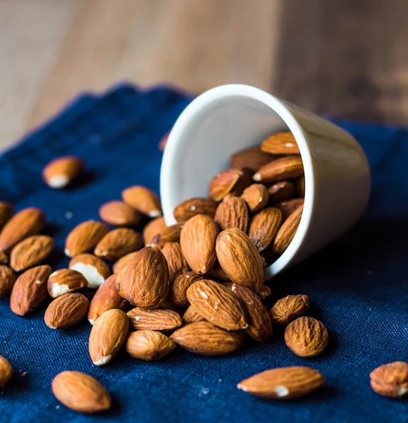 Scatter nuts almonds in a white bowl on blue napkin — Stock Photo, Image
