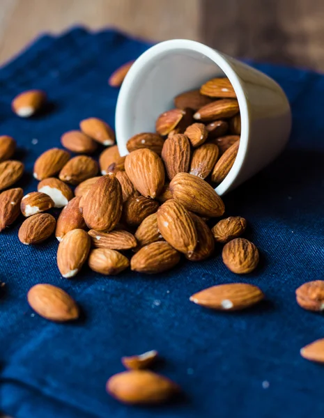 Scatter nuts almonds in a white bowl on blue napkin — Stock Photo, Image