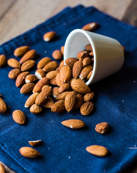 Scatter nuts almonds in a white bowl on blue napkin — Stock Photo, Image