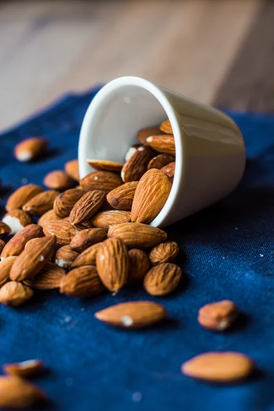 Scatter nuts almonds in a white bowl on blue napkin — Stock Photo, Image