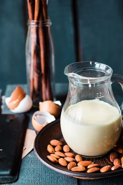 Gecondenseerde melk in een kruik glas, donkere amandelen op een plaat — Stockfoto