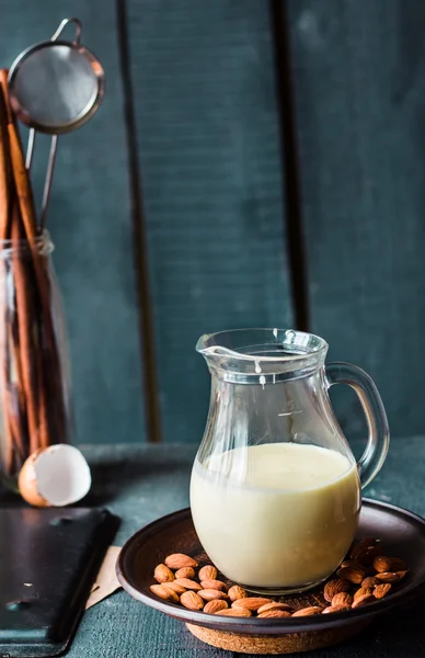 Gecondenseerde melk in een kruik glas, donkere amandelen op een plaat — Stockfoto