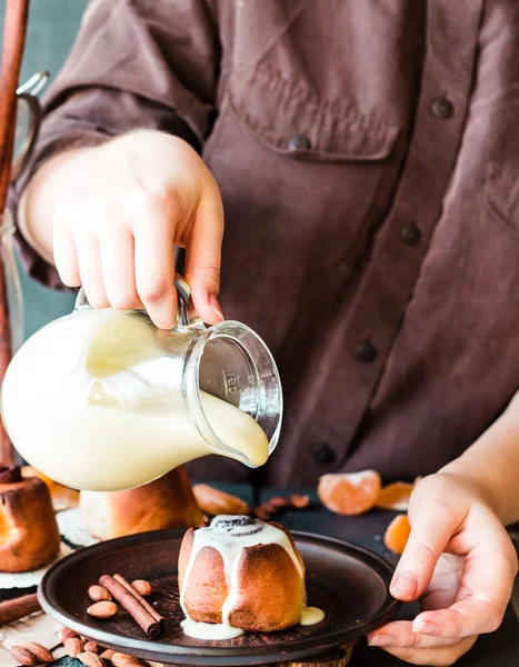 Cinnabon cinnamon rolls with cream sauce to pour, hands — Stock Photo, Image