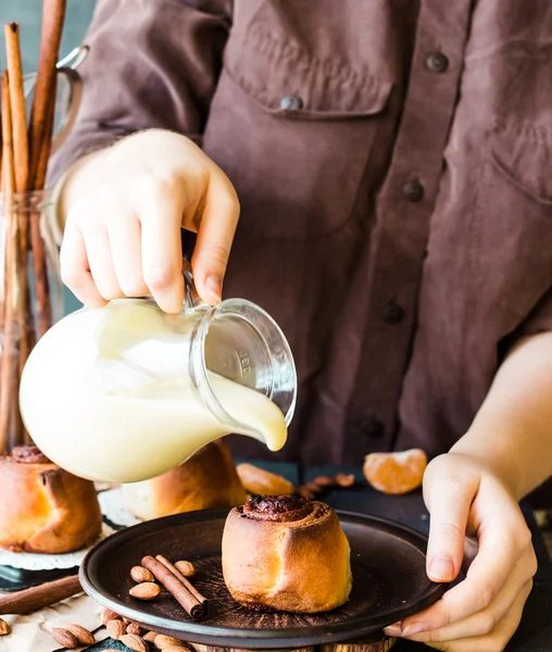 Cinnabon cinnamon rolls with cream sauce to pour, hands — Stock Photo, Image