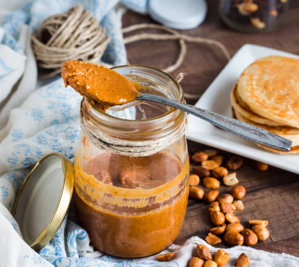 Erdnussbutter im Glas, einen Teelöffel und Pfannkuchen essen — Stockfoto