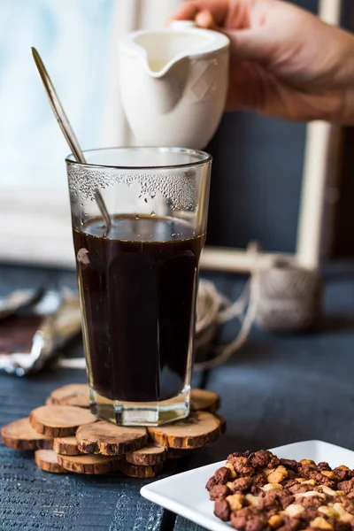 Milch zu schwarzer Kaffeetasse geben, Hand — Stockfoto