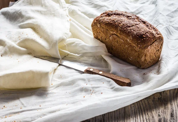 Fresh whole rye bread on a white linen tablecloth, knife — Stock Photo, Image