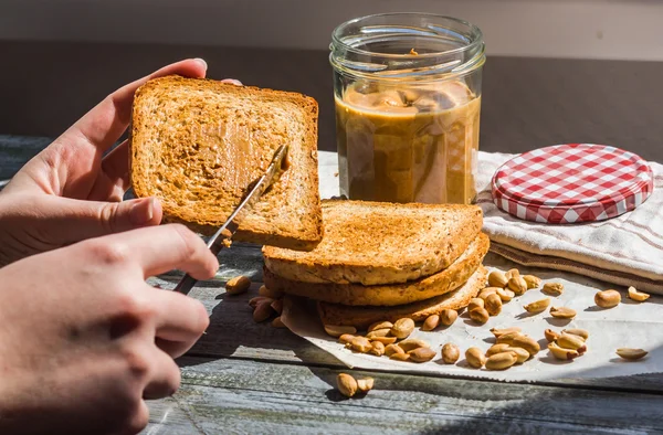 Adicionar a manteiga de amendoim de torrada rubicunda, mão, delicioso café da manhã — Fotografia de Stock