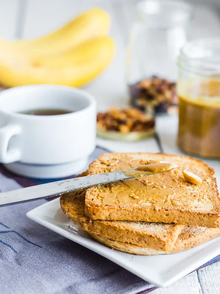 Rapea paahtoleipä maapähkinävoilla, banaaneilla, kahvilla, aamiaisella — kuvapankkivalokuva