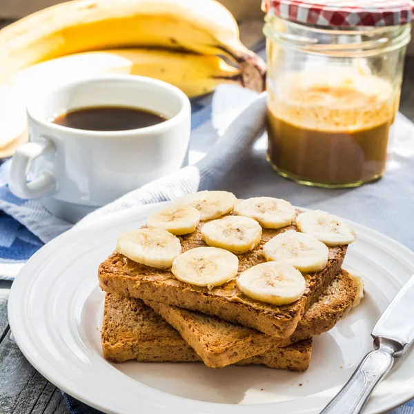 Грубые тосты с арахисовым маслом, нарезанные бананы, молоко, завтрак — стоковое фото