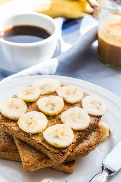 Грубые тосты с арахисовым маслом, нарезанные бананы, молоко, завтрак — стоковое фото