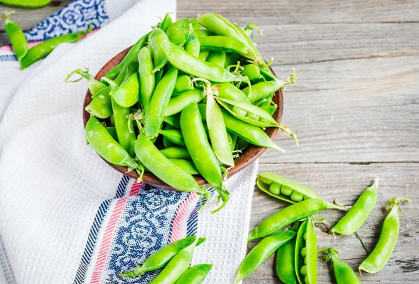 Guisantes verdes jóvenes en la vaina, plato de barro, fondo rústico — Foto de Stock