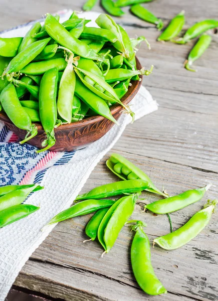 Guisantes verdes jóvenes en la vaina, plato de barro, fondo rústico — Foto de Stock