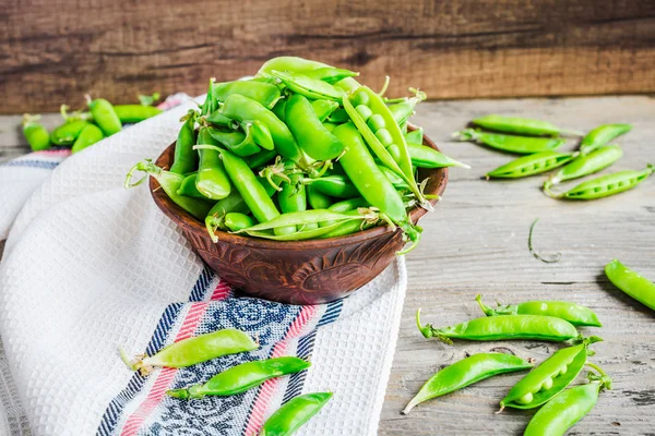 young green peas in the pod, earthenware dish, rustic background