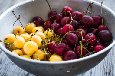 taze tatlı kiraz kırmızı ve sarı metal bir kevgir içinde