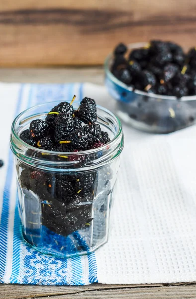 Mulberries pretas frescas em um frasco de vidro no backgro de madeira cinza — Fotografia de Stock