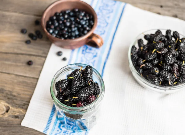 Mulberries pretas frescas em um frasco de vidro no backgro de madeira cinza — Fotografia de Stock