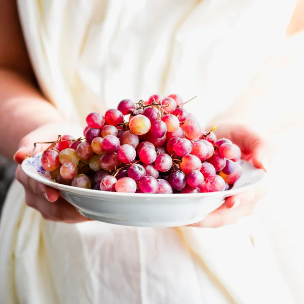 Hold in their hands a plate of fresh red grapes, raw fruits — Stock Photo, Image