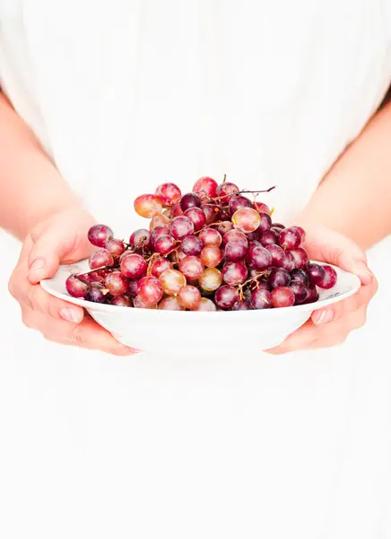 Segure em suas mãos um prato de uvas vermelhas frescas, frutas cruas — Fotografia de Stock