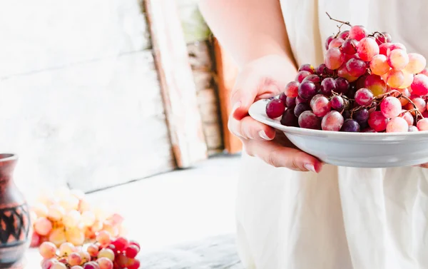 Sostenga en sus manos un plato de uvas rojas frescas, frutas crudas — Foto de Stock