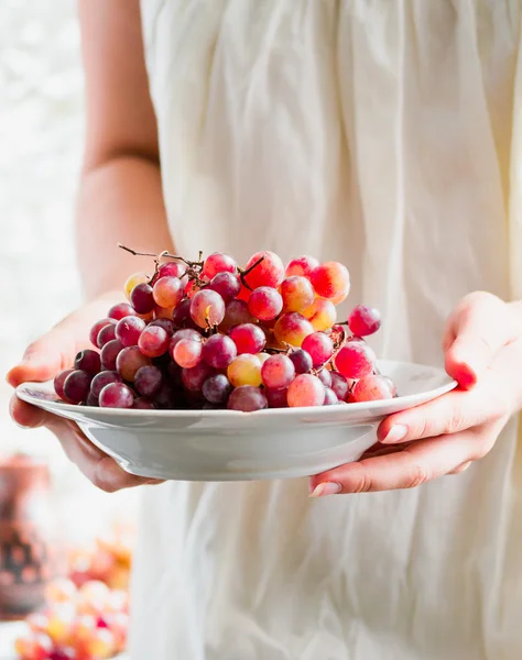 Tenez dans leurs mains une assiette de raisins rouges frais, fruits crus — Photo