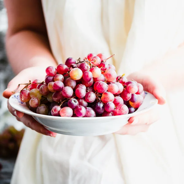 Hold in their hands a plate of fresh red grapes, raw fruits — Stock Photo, Image