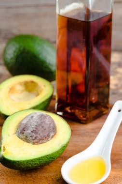 Avokado yarısı ve ahşap bir boa üzerinde cam şişede avokado yağı