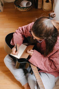 Gitarla müzik bestelerken deftere yazı yazan beyaz bir kadın.. 