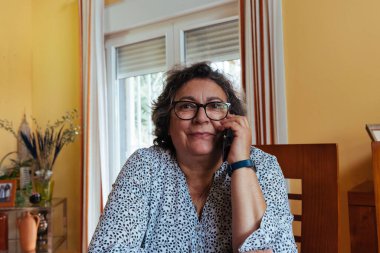 59 yaşında bir kadın cep telefonuyla konuşuyor. Ev konseptinde çalış.