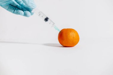 Beyaz arka planda mandalinaya iğne batıran bir şırıngayla el ele tutuşmak. Tıbbi konsept. Boşluğu kopyala.