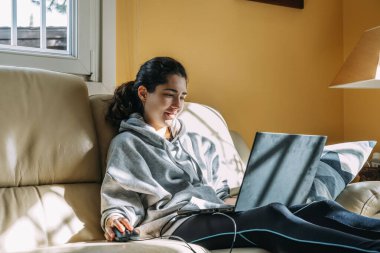 Evdeki kanepede bilgisayarla çalışan genç bir kadın. Ev konseptinde çalış