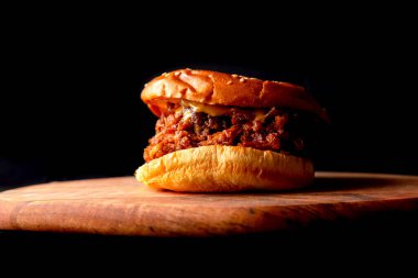 Siyah arkaplanlı, tahta bir tahtanın üzerinde kısmen yanmış bir çizburger. Fast food konsepti. Abur cubur.