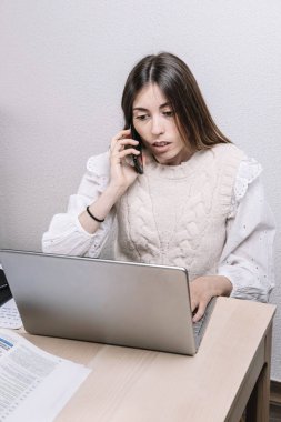 Bilgisayarı kullanıp cep telefonuyla konuşan genç bir kadın. Girişimci konsepti. Serbest meslek kavramı. Evde çalış..