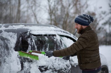 Bir adam kış günü arabasını bir fırçayla kardan temizliyor. 