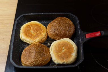Susamlı hamburger ekmeği ızgara tavada ısıtılıyor. Ev yapımı hamburgerler..