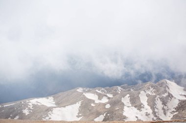 Karlı dağ zirveleri bulutlar ve sisle çevrilidir.