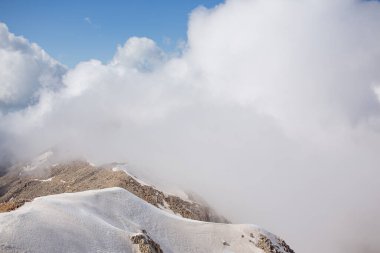 Karlı dağ zirveleri bulutlar ve sisle çevrilidir.