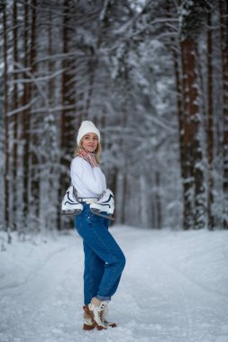 Kışın karlı ormanda elinde beyaz buz patenleriyle sarışın güzel bir kadın.. 