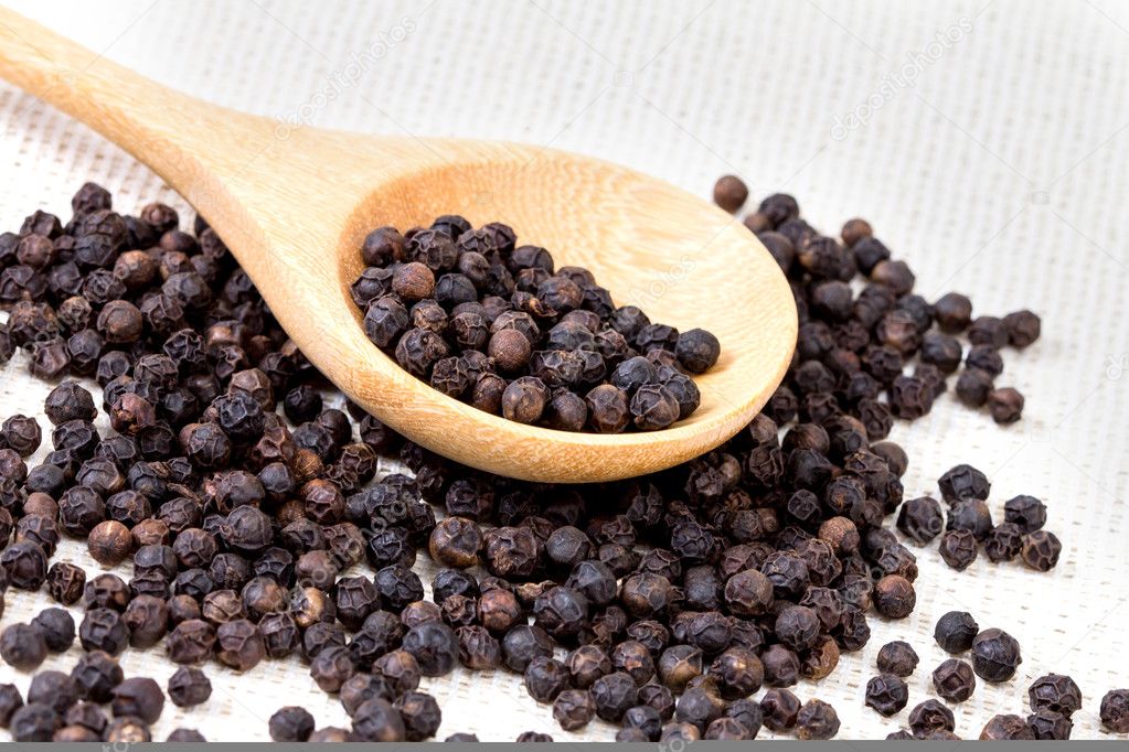 closeup black pepper in wooden spoon on fabric