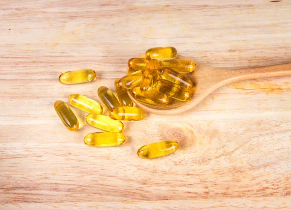 Closeup yellow soft gelatin supplement fish oil capsule on woode — Stock Photo, Image