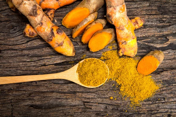 Poudre de curcuma dans la cuillère et les racines sur une assiette en bois — Photo