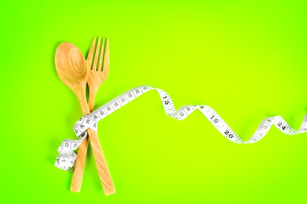 Wooden fork and spoon tied with Measuring tape on vibrant green — Stock Photo, Image