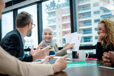 İş adamı, permalı kadın memurun başarılı şirketin hedefi hakkında sunum yaptığı belgeye bakıyor. O masanın üzerinde otururken o masanın arkasında duruyor..
