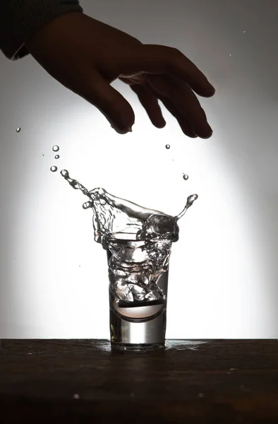 Splash in a glass. Vodka on an old wooden table as detailed close-up shot, Hand over glass