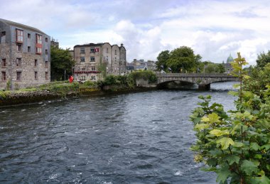 Taştan binalar ve köprünün yer aldığı tarihi bir İrlanda kasabasından akan bir nehrin manzarası.