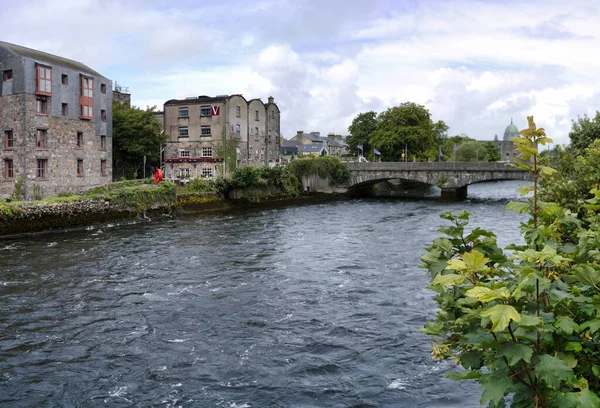 Taştan binalar ve köprünün yer aldığı tarihi bir İrlanda kasabasından akan bir nehrin manzarası.